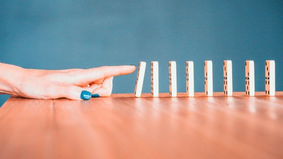A woman’s hand making a series of dominos topple.